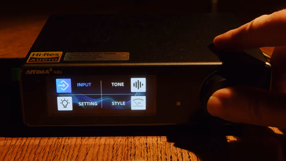 A finger on the knob beside the main menu screen showing Input, Tone, Setting and Style