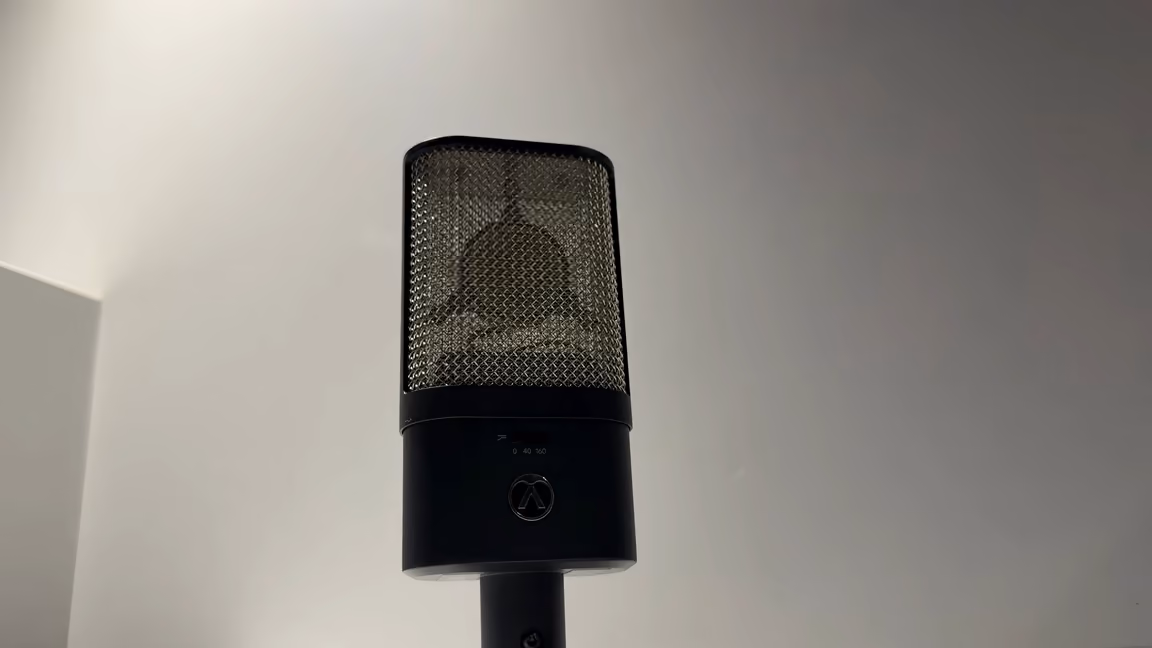 The Austrian Audio OC16 alone on a stand, front on: the flat black slab body, the Austrian Audio logo, the two-position high-pass switch above it, and the CKR6 capsule visible through the open mesh basket