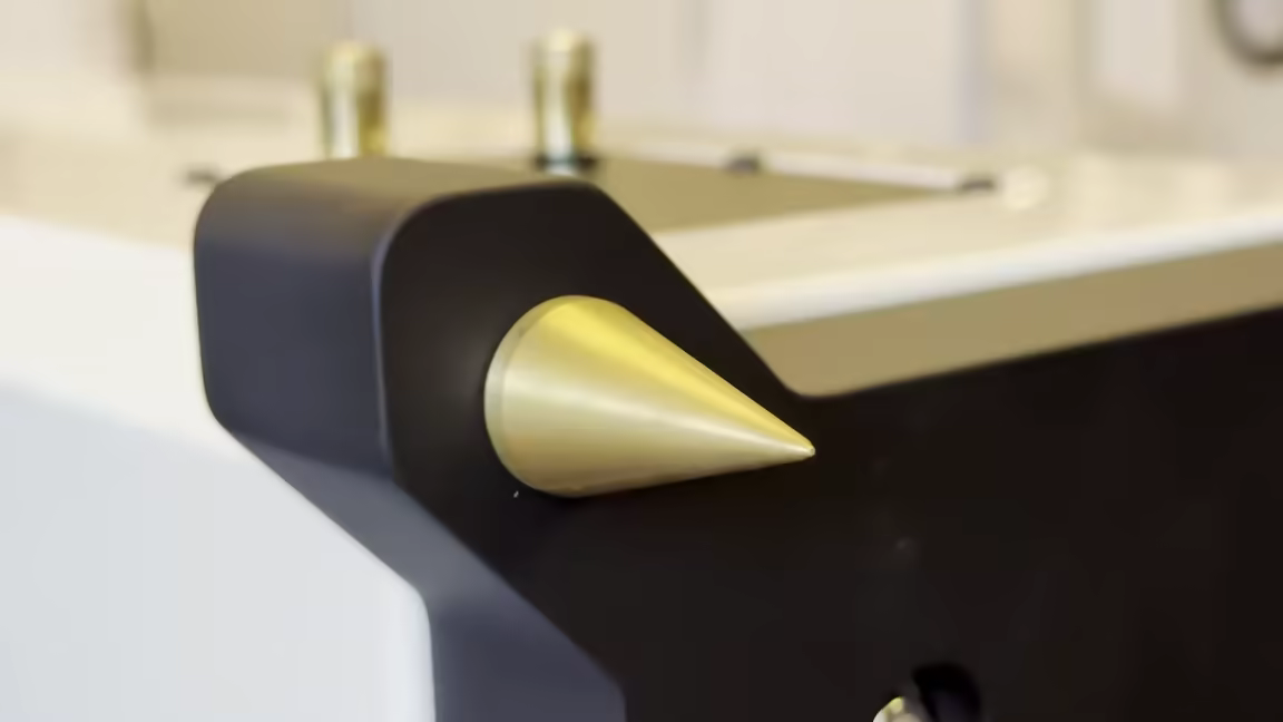 A sharp brass spike screwed into the Chors 5's base plinth, with the brass adjustment collars visible behind it