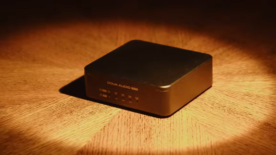 The Douk Audio U2 Pro, a small black aluminium box lit on a wooden desk, its front carrying the Douk Audio U2 Pro name above a row of PCM and DSD resolution indicator LEDs