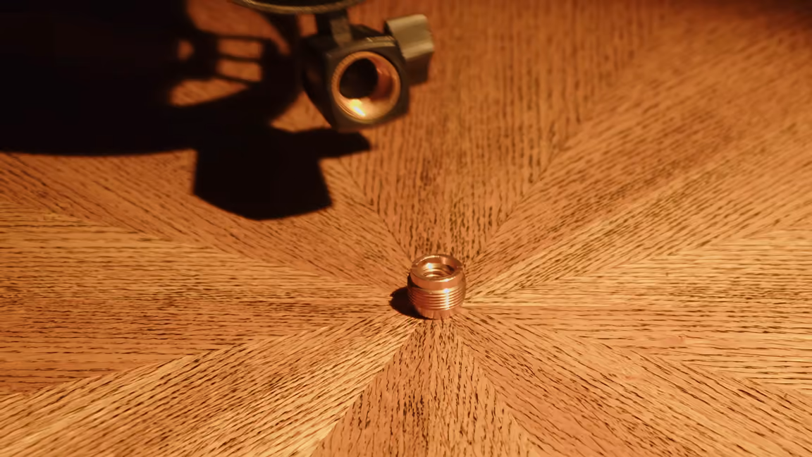 The included brass thread adapter lying on a wooden desk beside the K688's shock mount, whose threaded socket is visible above it