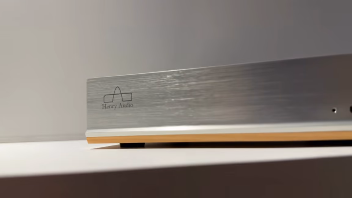 Close-up of the DA 256's front plate from a low angle, showing the brushed finish, the engraved Henry Audio logo, the single status LED and the wood base underneath