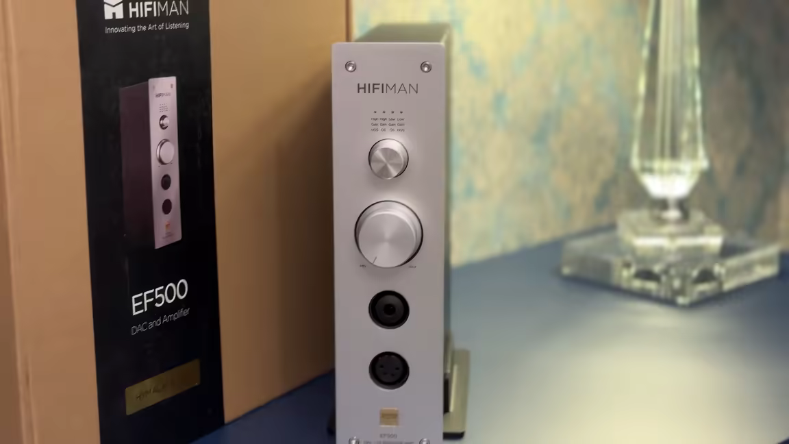The matte-silver HIFIMAN EF500 standing vertically beside its box, with its gain/oversampling selector, volume knob, and headphone outputs