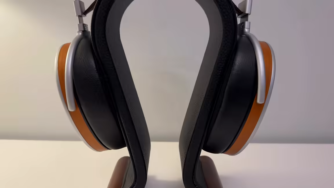 The HIFIMAN HE1000 Stealth on a stand, seen from the front: two large egg-shaped cups with black pads, wood-accent rims and silver frames, below the black-and-tan suspension headband