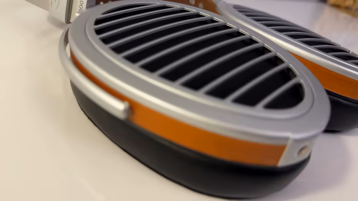 Macro of the HIFIMAN HE1000 Stealth's open-back ear cup: the patented Window Shade grille of curved metal slats over the driver, ringed by a silver frame and a wood accent band