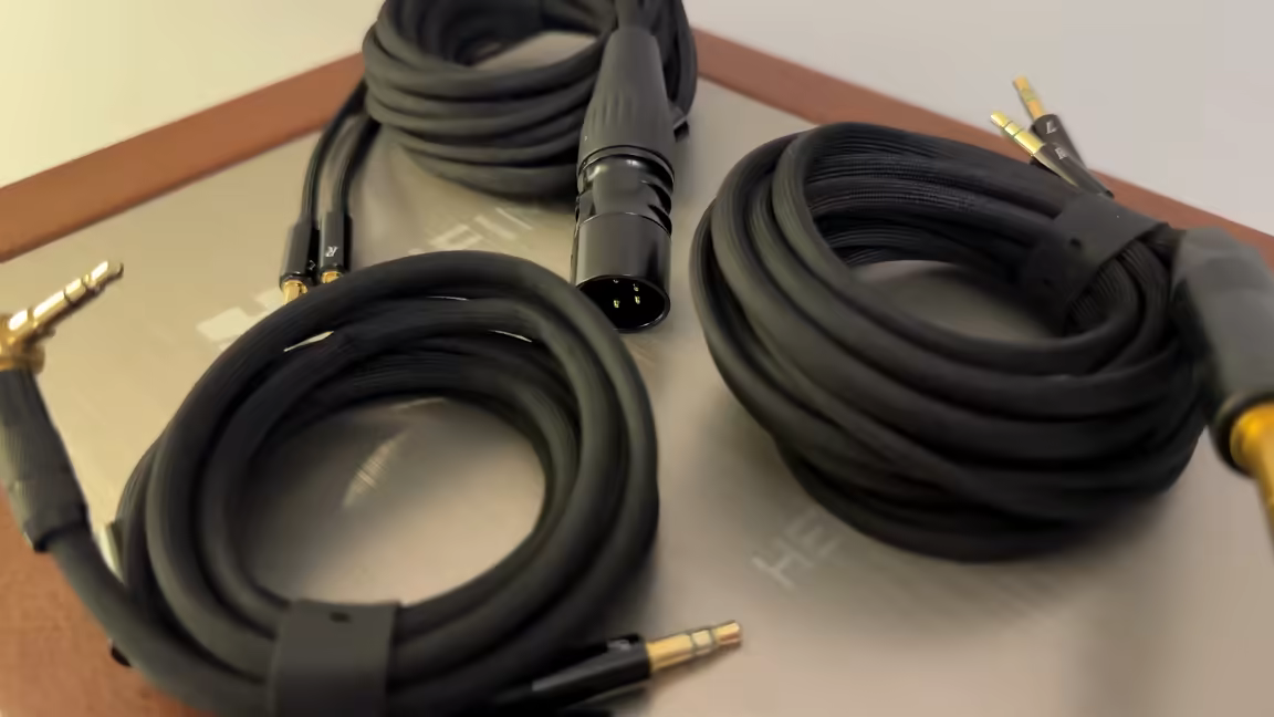 The HIFIMAN HE1000se's three included fabric-wrapped cables coiled on the leather presentation case: a balanced four-pin XLR, a quarter-inch plug for desktop gear, and a right-angle 3.5 mm for portable use, all black with gold-plated connectors