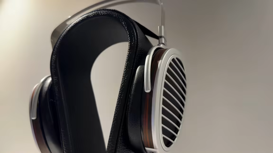 The HIFIMAN HE1000se in side profile on a stand: a large egg-shaped open-back planar cup with a silver aluminium frame, a wood-veneer rim and the Window Shade grille, hanging below the black leather suspension headband