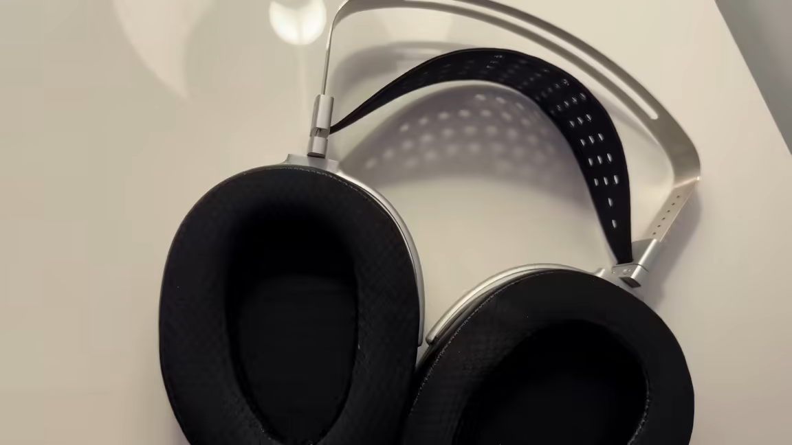 Top-down view of the HIFIMAN HE1000se's two deep ear pads and headband: angled hybrid pads with a black perforated cloth contact face, beside the silver perforated metal headband arc