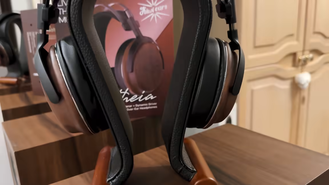 The full Kiwi Ears Atheia open-back headphone on a wooden stand, showing both walnut earcups, the leather suspension headband, and aluminium yokes, with its retail box behind