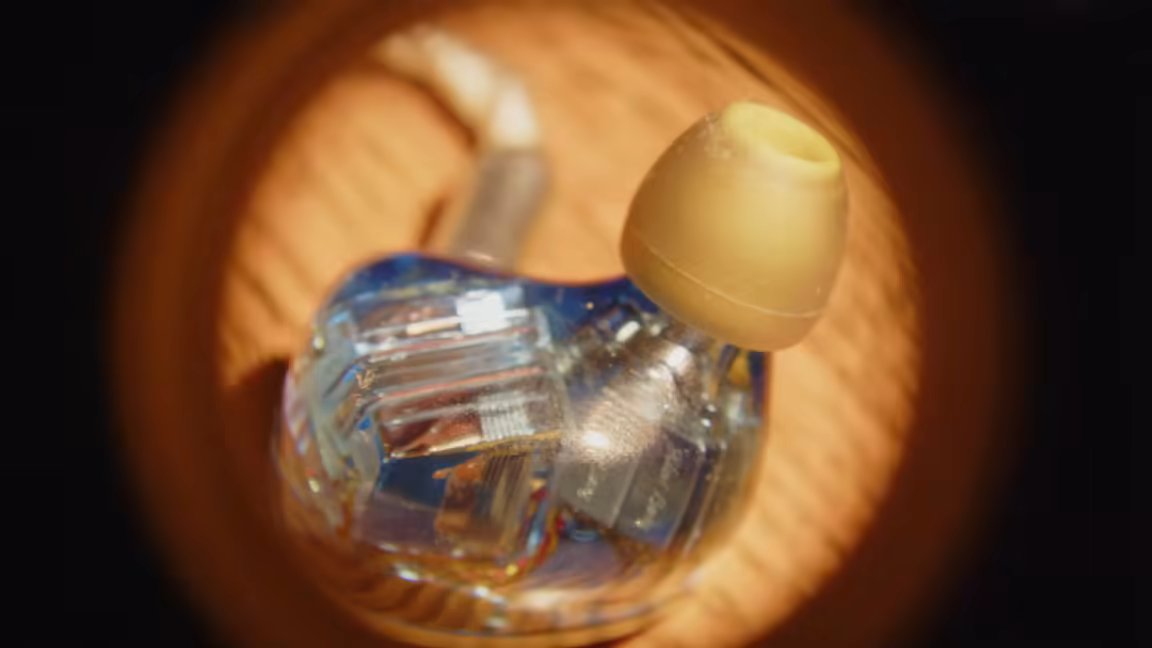 Macro of the Kiwi Ears Orchestra II's clear resin shell, exposing the stacked balanced-armature drivers and wiring, with an ear tip on