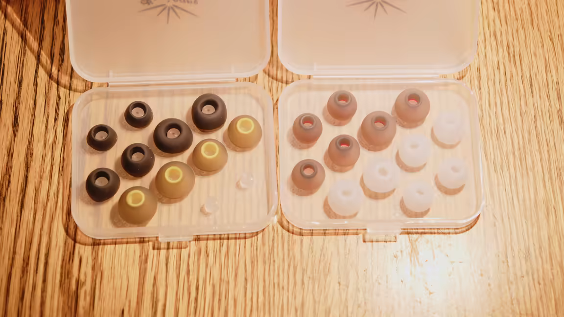 Two open cases of Kiwi Ears ear tips in different colours and core densities on a wood table