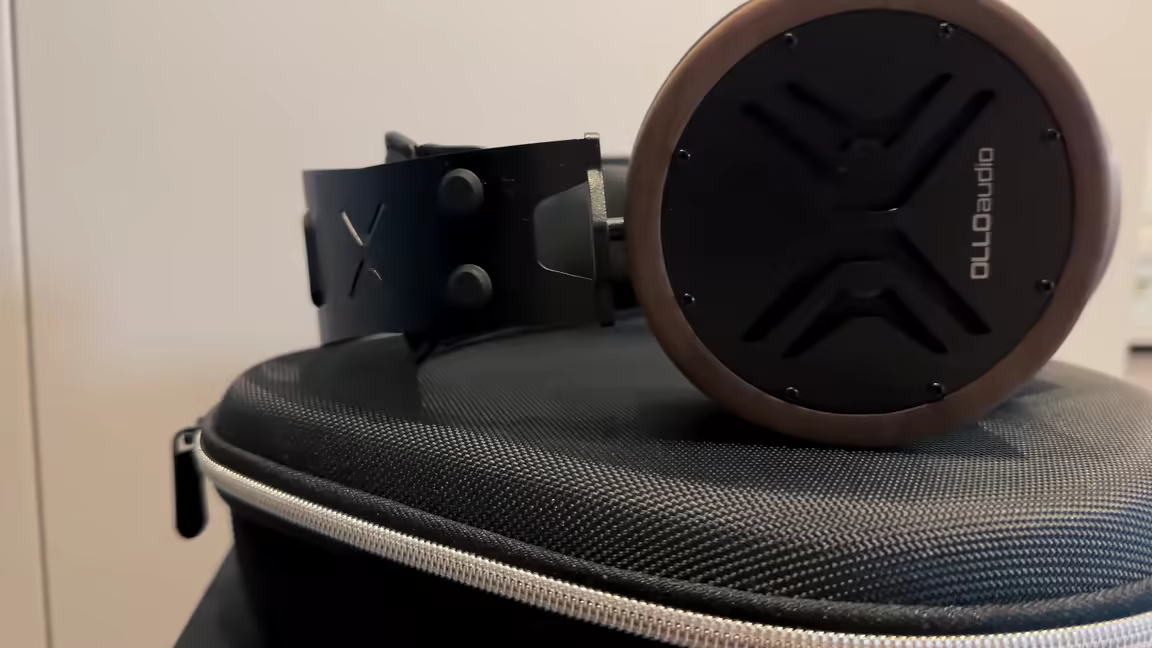The OLLO Audio X1's steel suspension headband with X cutout, resting on its hard carrying case