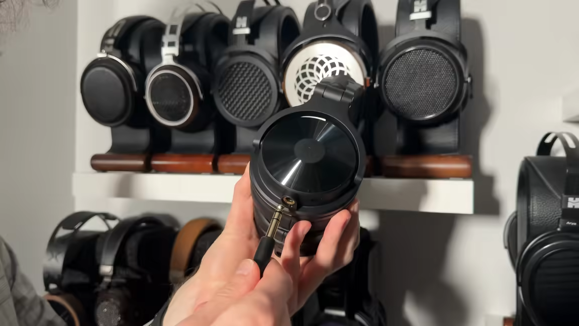 A cable plugged into one of the OneOdio Max 1's built-in analog jacks on the glossy vinyl-textured earcup
