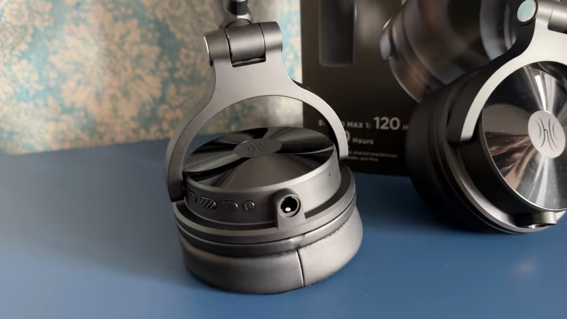 The OneOdio Max 1's earcup swivelled flat for storage, showing the on-cup control buttons and analog jack
