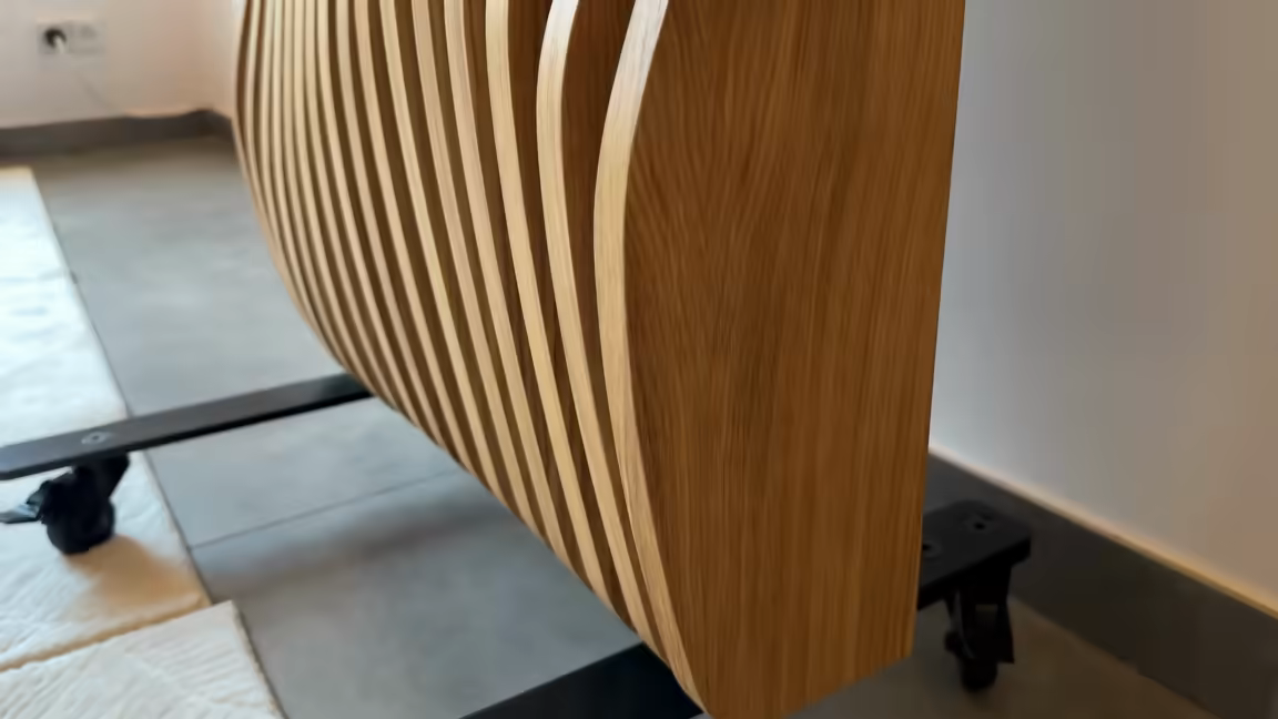 Low-angle view of the tower's black steel foot rail with a caster wheel at each end, the slim oak body rising above it