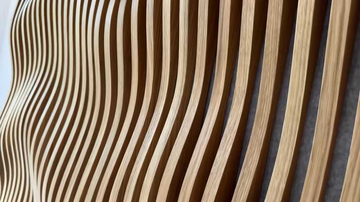 Raking-light macro along the oak slats, each one set at a different depth and curve so the surface reads as a rippling wave