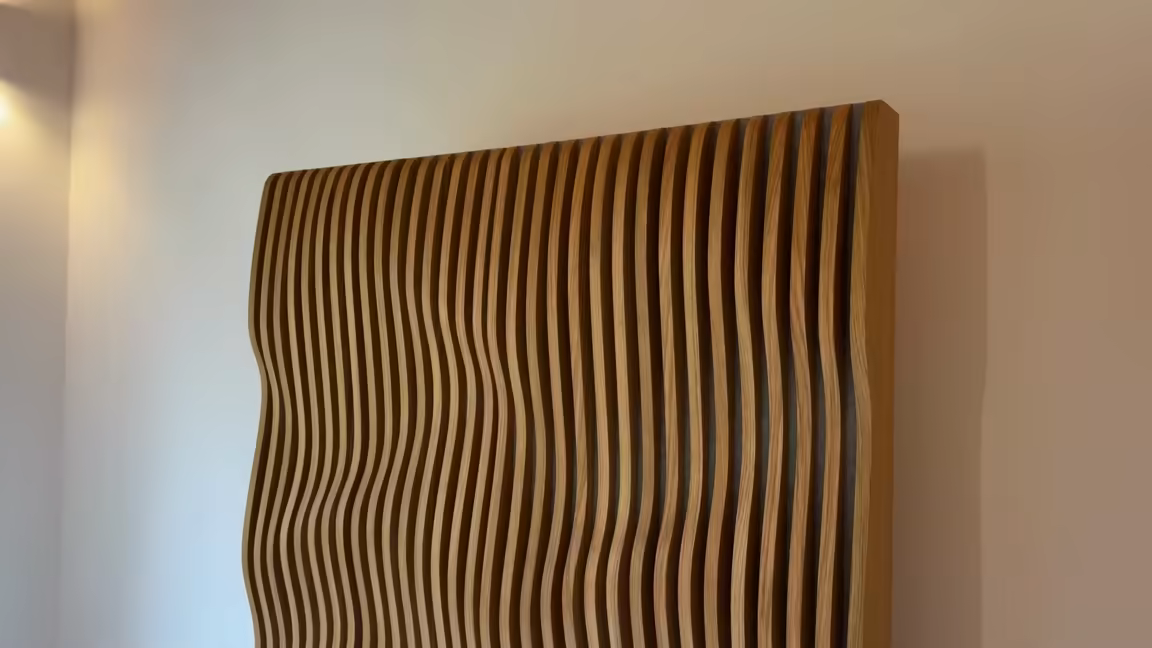 The top corner of an ORTVIK Parametric Tower in natural oak, its wavy slats standing proud of the panel against a plain wall