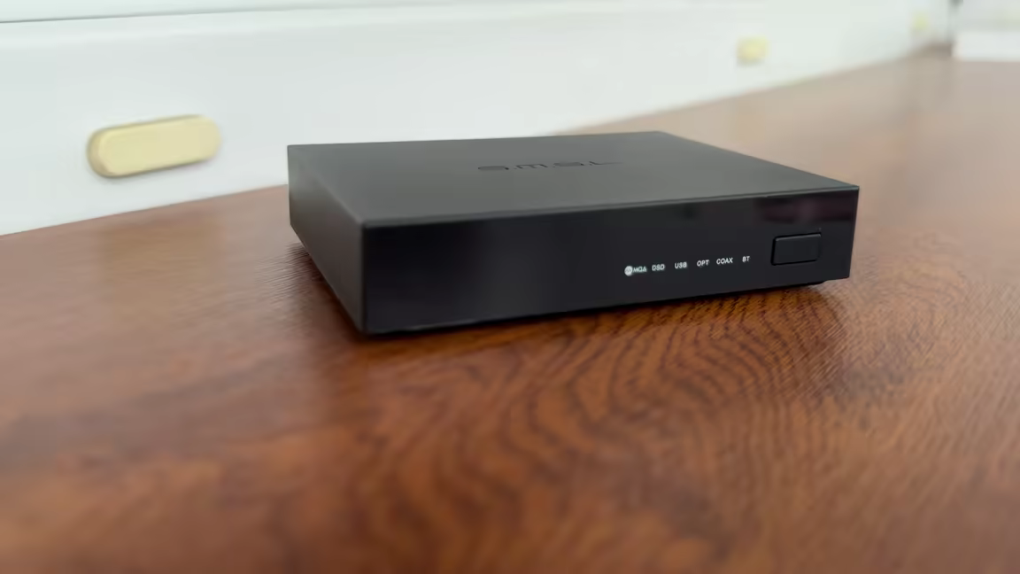 The SMSL PS200's small black chassis with its front LED input indicators, control button, and engraved top logo