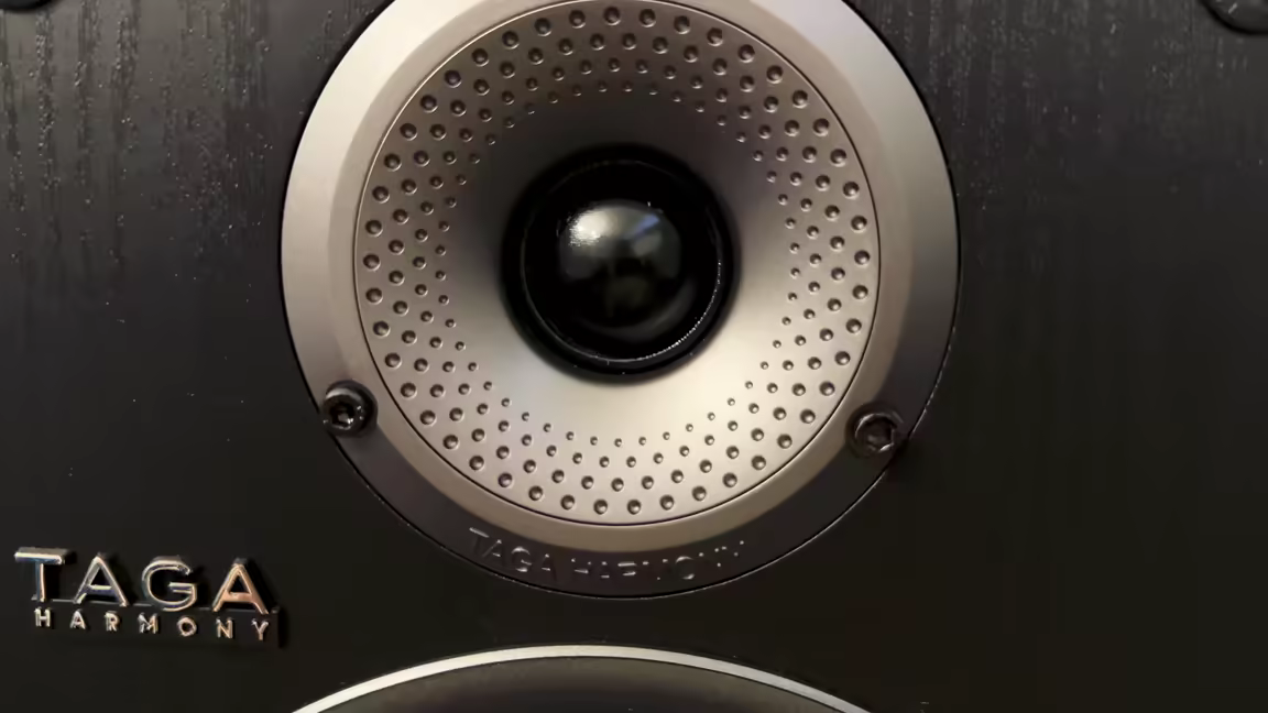 Close-up of the 1-inch silk dome tweeter set in its perforated concave-diffuser waveguide, beside the Taga Harmony logo