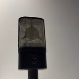 The Austrian Audio OC16 alone on a stand, front on: the flat black slab body, the Austrian Audio logo, the two-position high-pass switch above it, and the CKR6 capsule visible through the open mesh basket