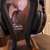 The full Kiwi Ears Atheia open-back headphone on a wooden stand, showing both walnut earcups, the leather suspension headband, and aluminium yokes, with its retail box behind