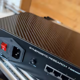 Synergistic Research Network Router UEF from a rear corner, carbon fiber lid above the inlet and ports