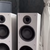 The pair of Taga TAV-607F floor-standers with grilles off, showing the three-way layout: tweeter, midrange driver, and 6.5-inch woofer