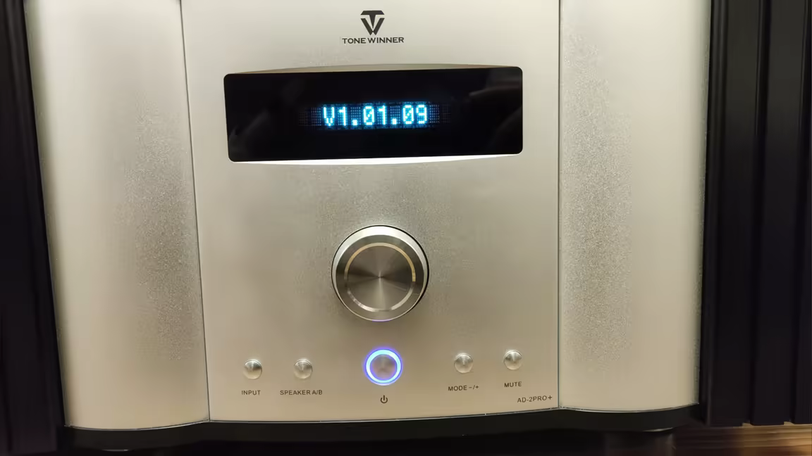 The AD-2PRO+'s silver front panel: the blue LED screen above the volume knob and a row of input, speaker A/B, power, mode, and mute buttons